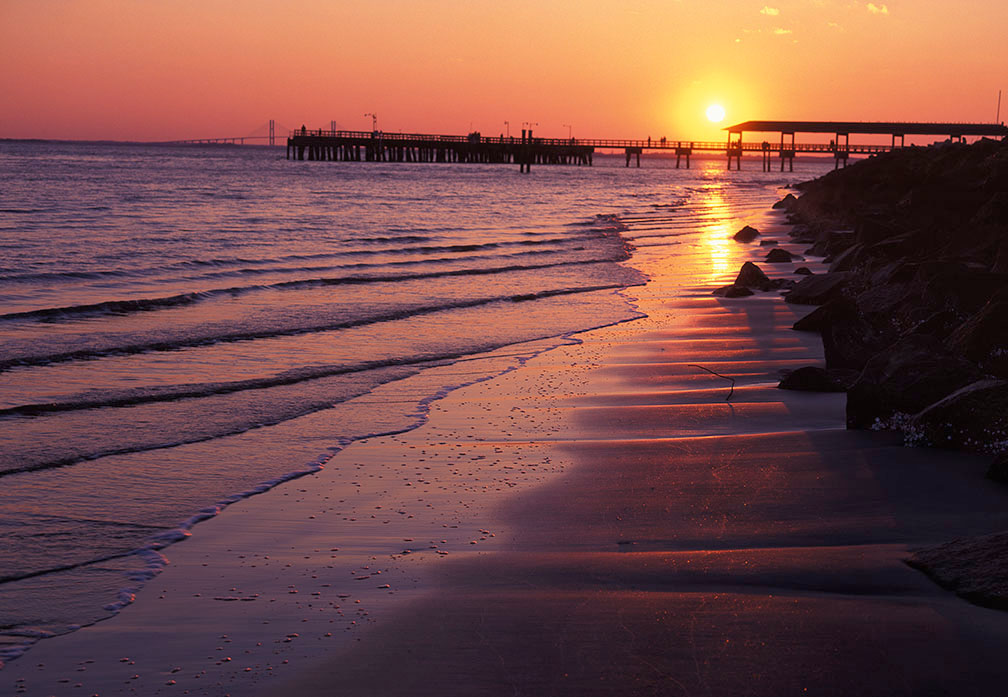 Sun setting above a pier illuminates a shoreline with golden light