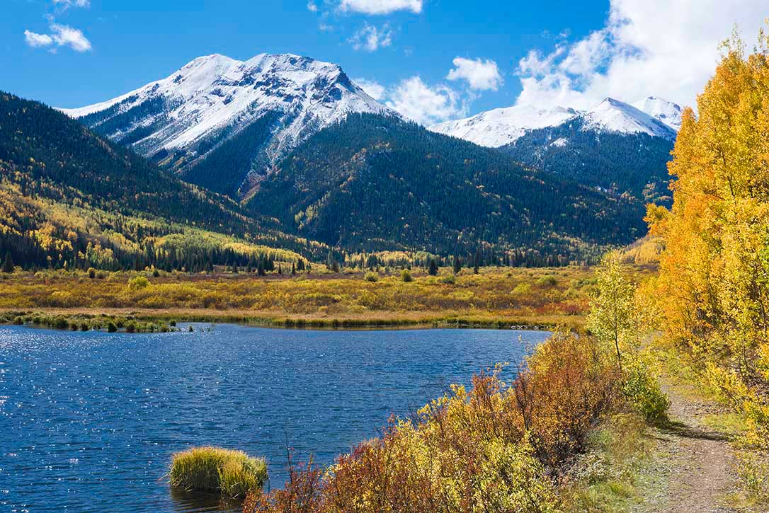 Golden autumn foliage surrounds Crystal Lake with snow covered mountains south of Ouray, CO